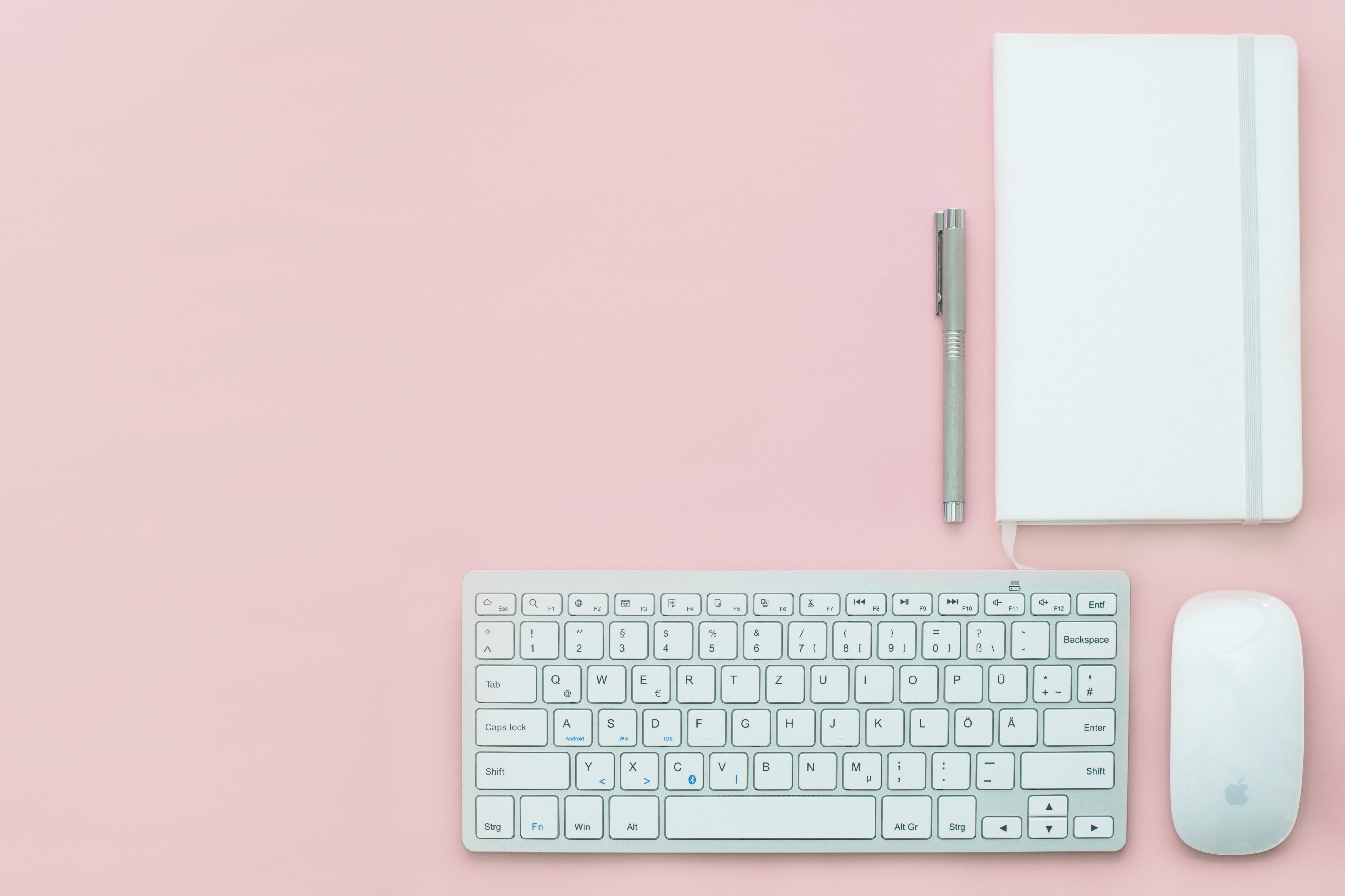 Keyboard, mouse and notepad on pink background